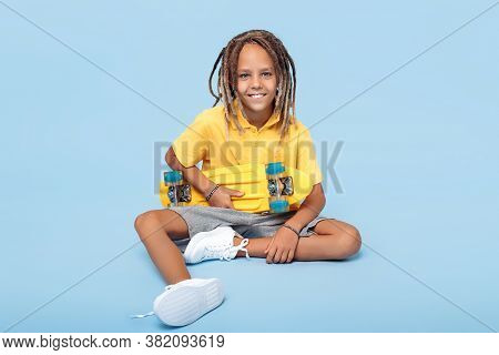 Cheerful Little Boy With African Dreads With Skateboard On The Blue Background.