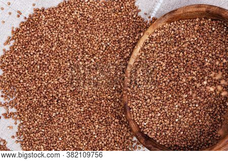 Raw Roasted Buckwheats From Round Wooden Bowl Pour On Cloth Surface. Russian Grechka. Organic Health