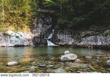 Rindbach Waterfall With Wooden Bridge, Forest And Small Lake. Austria Alps Mountain