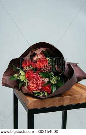 Bouquet Of Flowers In Burgundy Package On Wooden Chair On Light Background. Rosa, Skimmy, Carnation,