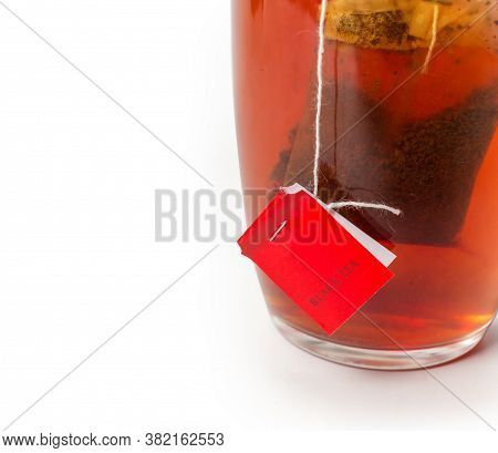 Bag Of Black Tea With Red Label In The Glass Cup With Freshly Brewed Tea On A White Background, Frag