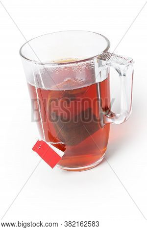 Glass Cup Of Freshly Brewed Black Tea From Tea Bag With Red Label On A White Background