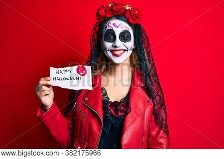 Woman wearing day of the dead costume holding happy halloween paper looking positive and happy standing and smiling with a confident smile showing teeth 