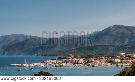 A Flying Boat Soars Above The Bay And Citadel At Saint Florent In Corsica With Cap Corse In The Dist