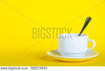 White Cup With Saucer Teaspoon On Yellow Background