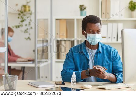 Portrait Of Young African-american Man Wearing Face Mask And Sanitizing Hands While Working In Cubic