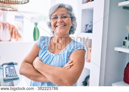 Middle age shop assistance woman working at the counter of retail shop smiling happy
