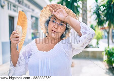 Middle age woman with grey hair using handfan on a very hot day of a heat wave