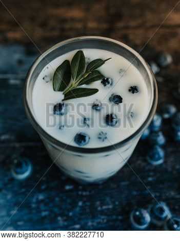Blueberries Float In A Transparent Glass With Milk. Green Basil Leaves In A Glass