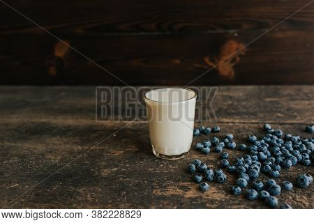 A Transparent Glass With Milk. Blue Fresh Blueberries Are Scattered