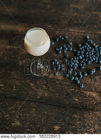 A Transparent Glass With Milk. Blue Fresh Blueberries Are Scattered