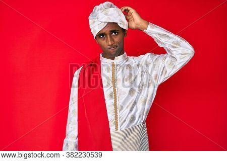 Handsome indian man wearing tradition sherwani clothes confuse and wonder about question. uncertain with doubt, thinking with hand on head. pensive concept. 