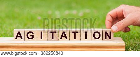 Man Hand Holding Wooden Cube Block With Agitation Business Word On Green Lawn Background