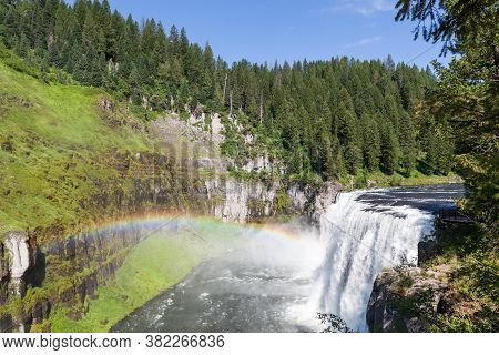 A Rainbow In The Mist Of Upper Mesa Falls As It Cascades Over A Cliff In The Rugged Wilderness Of He