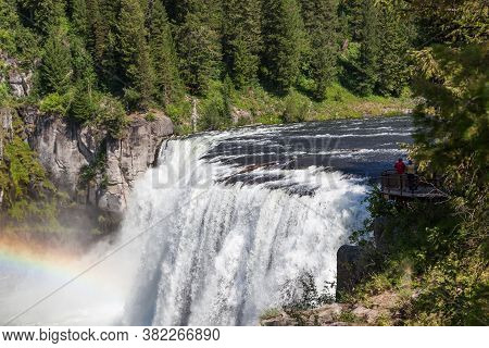 A Rainbow In The Mist Of Upper Mesa Falls As It Cascades Over A Cliff In The Rugged Wilderness Of He