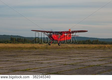 A Vintage Red Stinson Small Plane Flies Low Over A Private Concrete Runway.