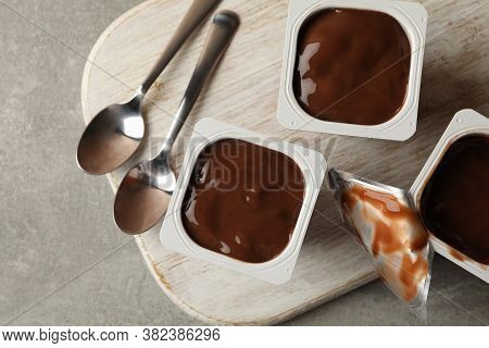 Board With Plastic Cups Of Yogurt And Spoons On Gray Background
