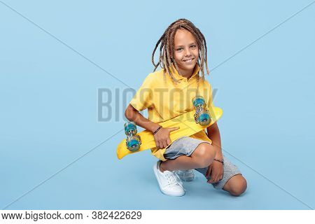 Cute Little Boy With African Dreads Holding Skateboard And Smile Over Blue Background.