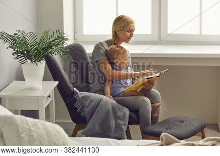 Mother And Child Toddler Reads A Story In A Book In A Room With A Window. Mothers Day.