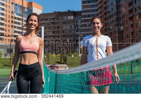 Two Smiling Caucasian Women On A Tennis Court On A Sunny Summer Day.