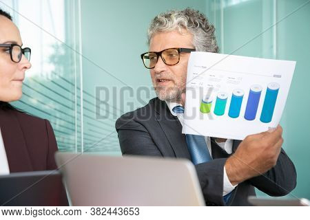 Executive Presenting Paper Report At Meeting. Grey Haired Man In Suit Showing Document With Growth C