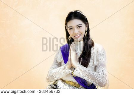 Asian Woman In Thai Traditional Vintage Costume Siting And Greeting Action On Brown Background. Gree