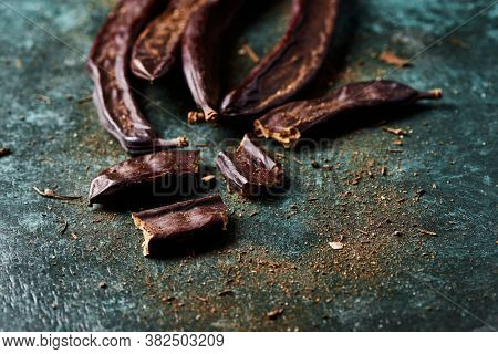 closeup of some ripe carob beans on a rustic dark green surface