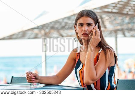 Communication. Portarit Of A Stylish Woman With A Scared Look Is Sitting In A Summer Cafe On The Bea