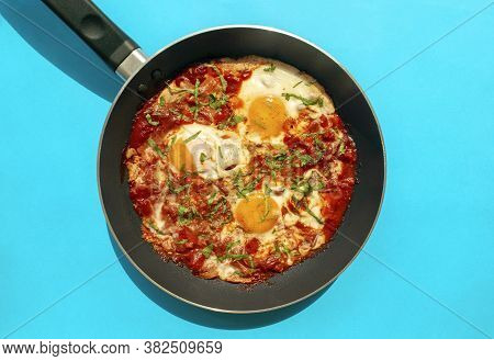 Shakshuka - Poached Eggs In Tomato Sauce, Onion, Pepper And In Iron Pan On Blue Bright Background. F