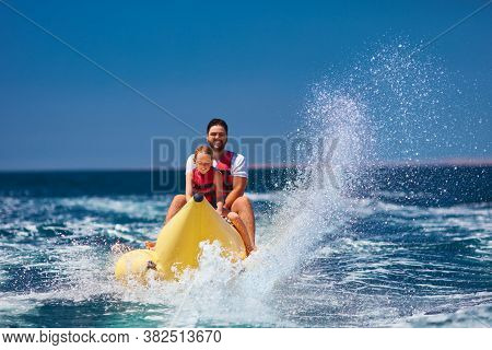 Happy Family, Delighted Father And Son Having Fun, Riding On Banana Boat During Summer Vacation