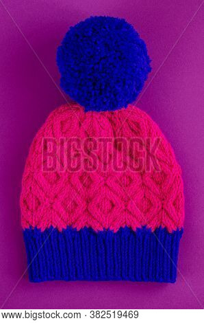 Beautiful Two Color Handknitted Hat With Pompon On Purple Background. Top View