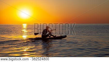 Silhouette Of A Man Floating On A Board With An Oar. Dawn Sun On The Sea. Swimming On A Supboard. Wa