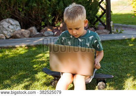The Boy Is Sitting On The Grass And Studying On A Laptop. Concept Of Remote Learning, Home Learning,