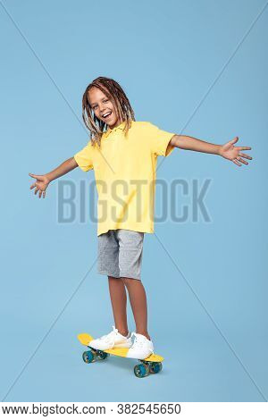 Gleeful Little Boy With African Dreads On Skateboard Having Fun Over Blue Background.