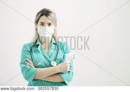 Female Doctor Or Nurse At Hospital Holds Pyrometer In Hand. Safety Measures Against The Coronavirus.