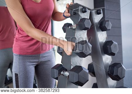 Close Up Of Girls Wearing Sportswear Standing In The Gym Choosing The Weight Of The Dumbbell.  Exerc