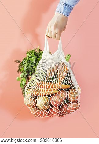 Mesh Bag With Vegetables And Herbs In Female Hand. Woman Hold String Net Shopping Bag On Pink Backgr