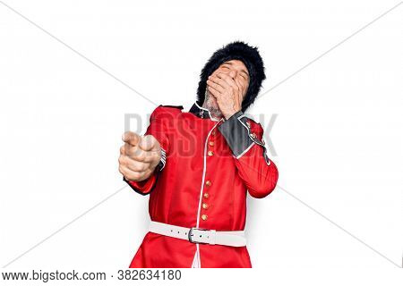 Middle age handsome wales guard man wearing traditional uniform over white background laughing at you, pointing finger to the camera with hand over body, shame expression