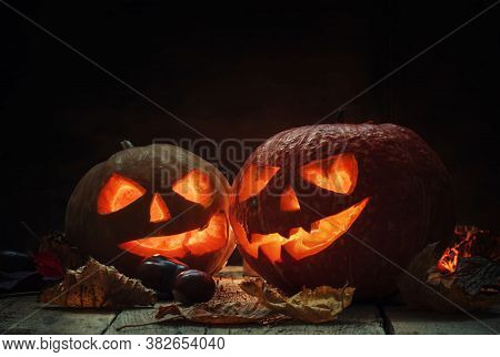 Two Halloween Pumpkin Jack-o-lantern On Dark Wooden Background With Fallen Leaves And Flames, Select