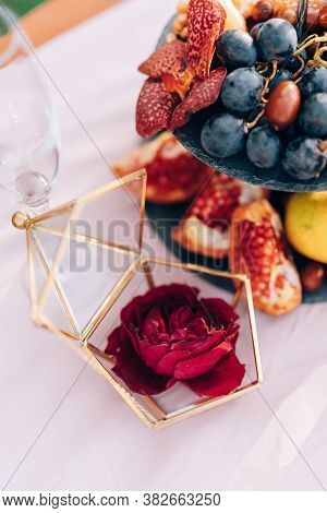 Rose In A Case, A Box For Rings, On A Table With A Whatnot With Grapes And Pomegranates At A Wedding