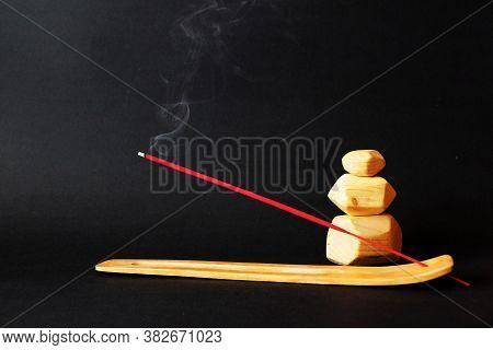 Smoking Incense Stick On Wooden Stand And Wooden Tumi Ishi On Black Background.