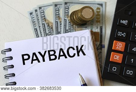 Payback Word In A Notebook With A Pen Against The Background Of Dollar Bills. Business And Finance C