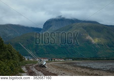 Sea Yacht Lying On The Shore On The Background A High Cloud-covered Mountain Ben Nevis. Loch Linnhe 