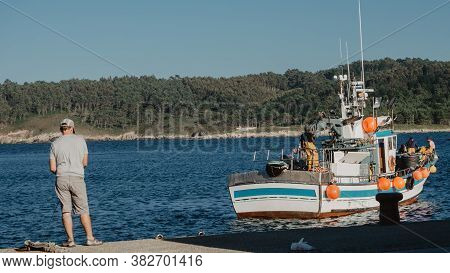 Muxia, A Coruña, Spain: 08/15/2018: Scene Of An Angler And A Fishing Boat With Fishermen On Board