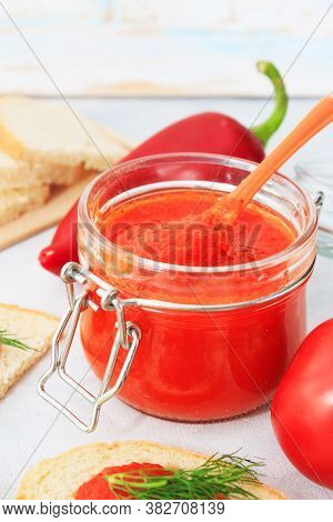 Ajvar, Pepper Mousse In A Jar And On  Bread And Gray Backgground. Ajvar - Delicious Dish Of Red Pepp