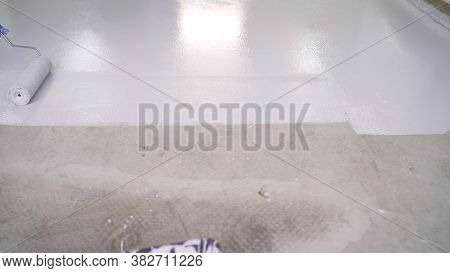 Floor Painting. Dirty Repairs And Alterations. A Worker Paints The Floor White With A Roller. The Co