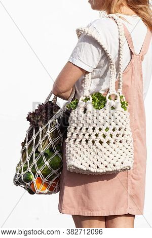 Young Woman In Light Summer Clothes Is Holding Mesh Shopping Bag With Vegetables, Greens Without Pla