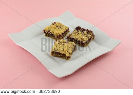 Three Baked Raspberry Oat Crumble Squares On White Dessert Plate On Pink Background