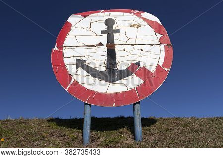 Round Sign With A Red Color And An Anchor Drawn Inside, Installed On The Bank Of A River Or Lake In 