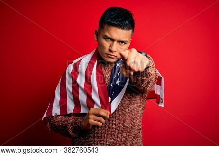 Young handsome latin patriotic man wearing united states of america falg pointing with finger to the camera and to you, hand sign, positive and confident gesture from the front